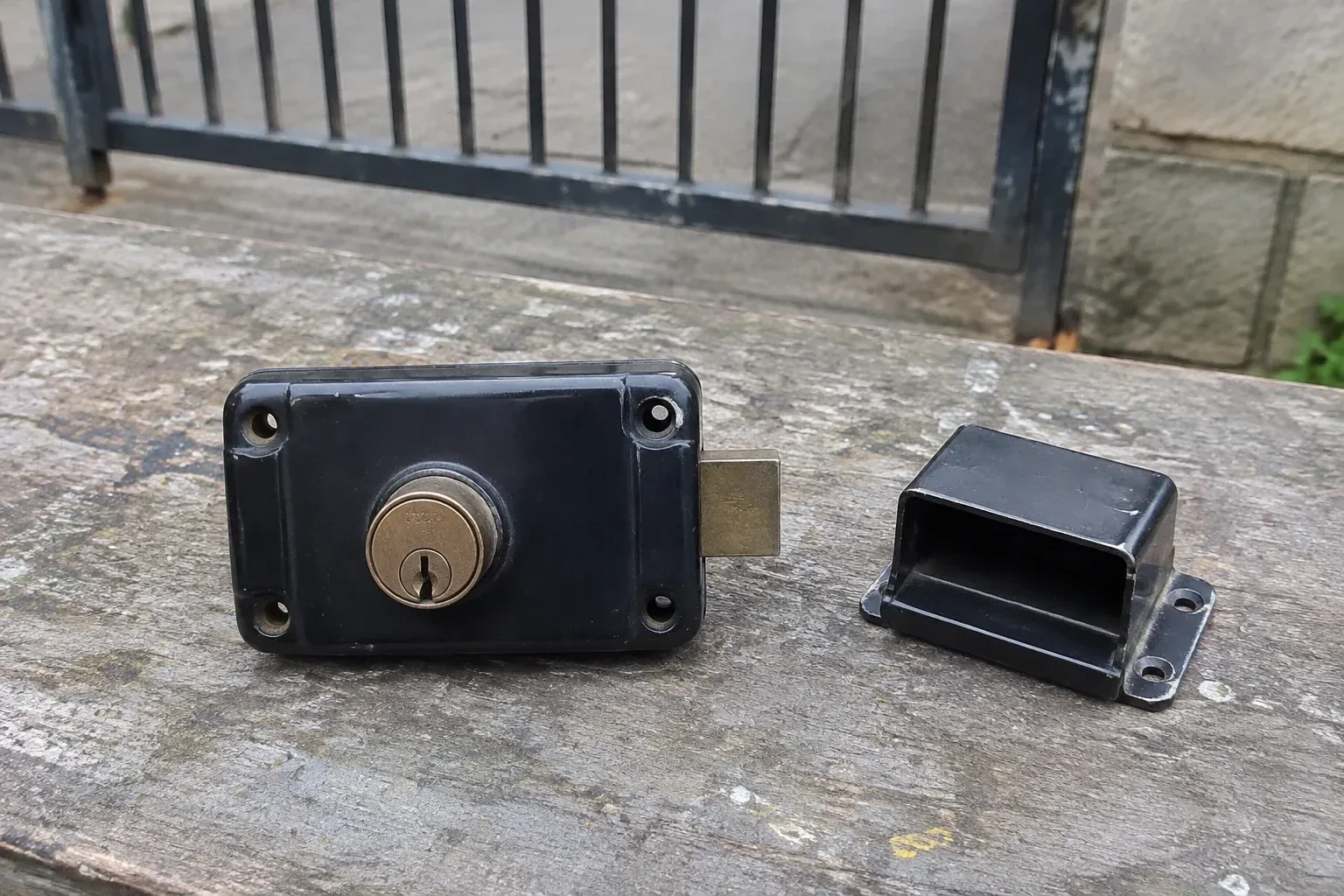 Detached rim gate lock and separate box keeper on an outdoor workbench. — Gate & Building Entry Locks, Mississauga